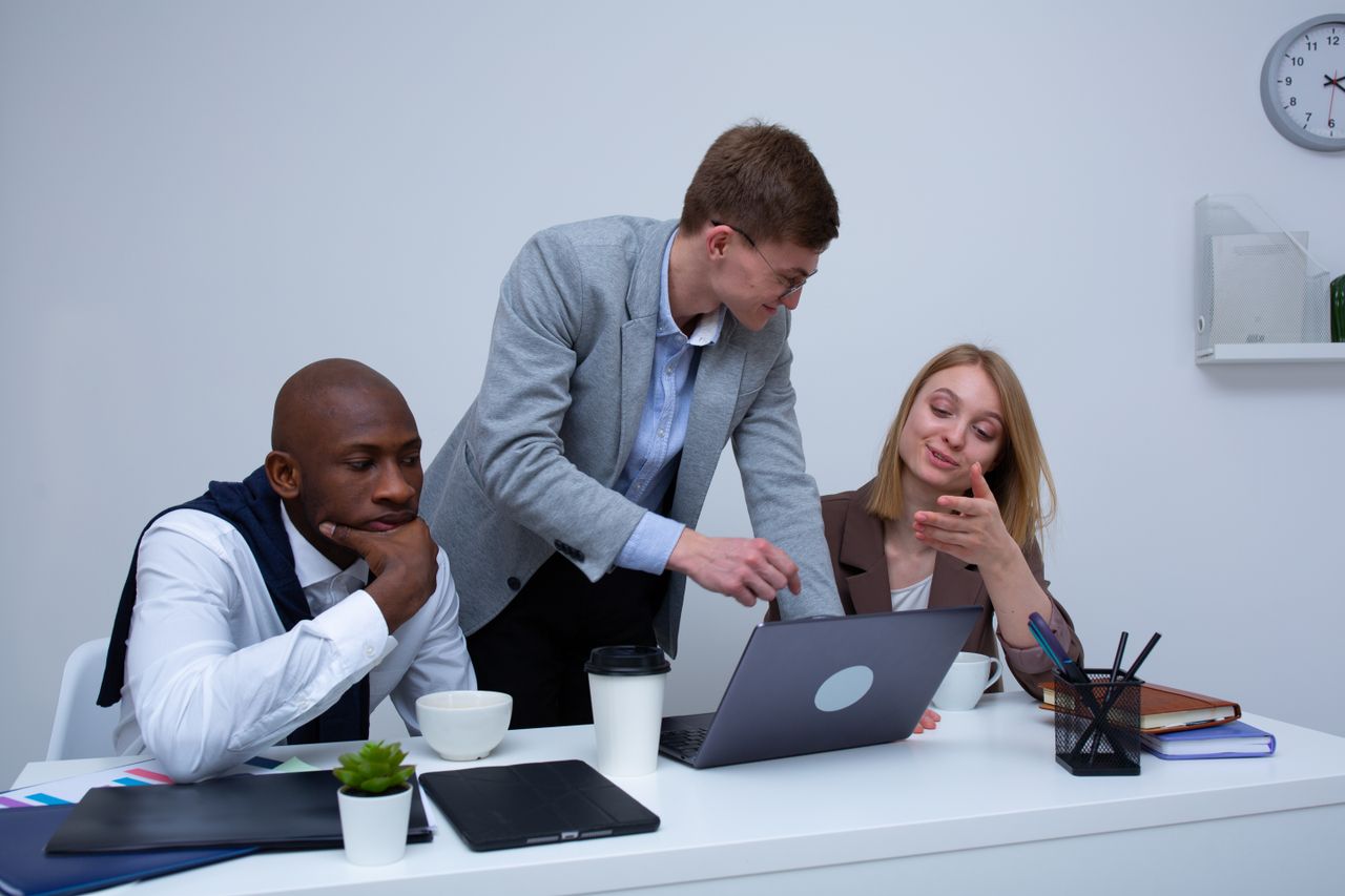 testimonials-img A diverse team collaborating in a modern office environment, discussing work on a laptop.