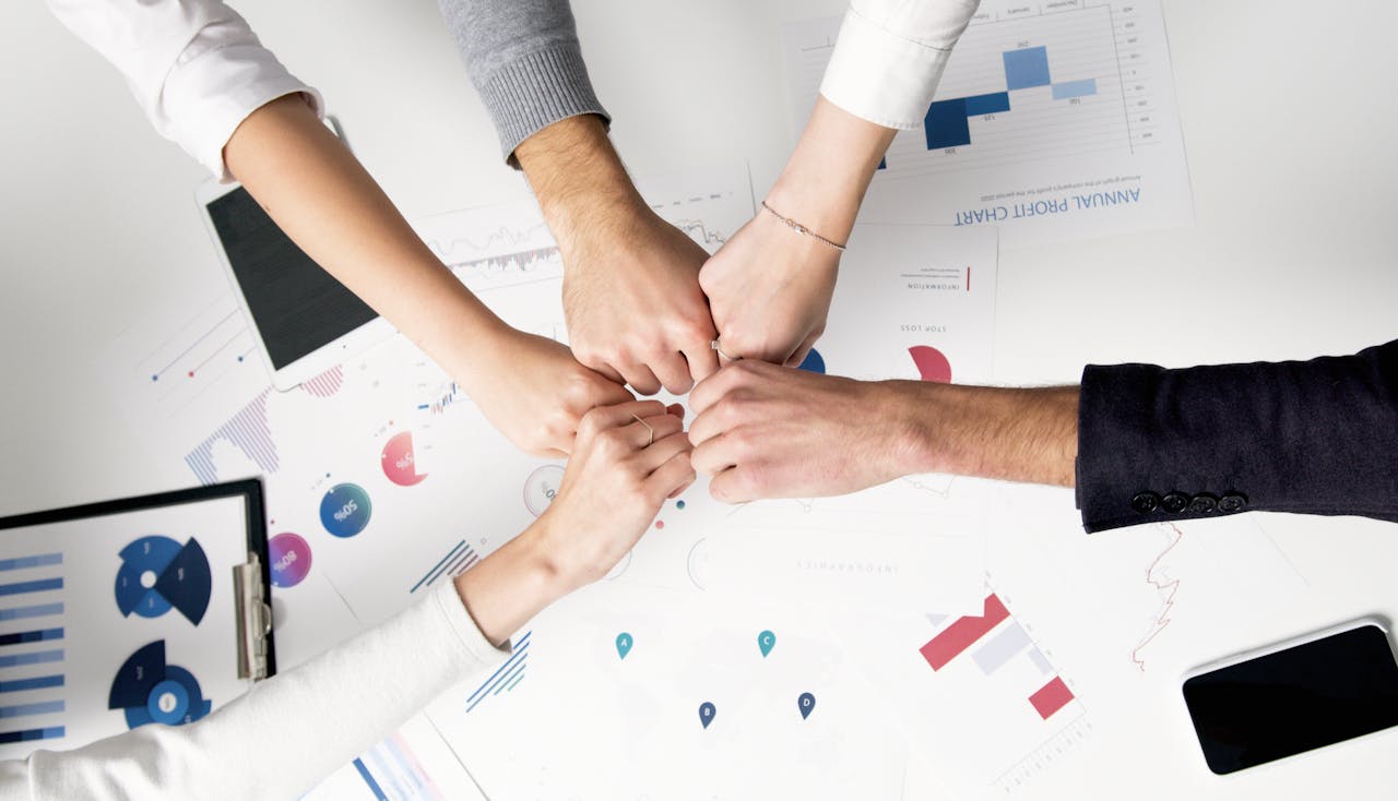 home-hero-bg Colleagues celebrate success with a fist bump over financial charts depicting teamwork and unity.